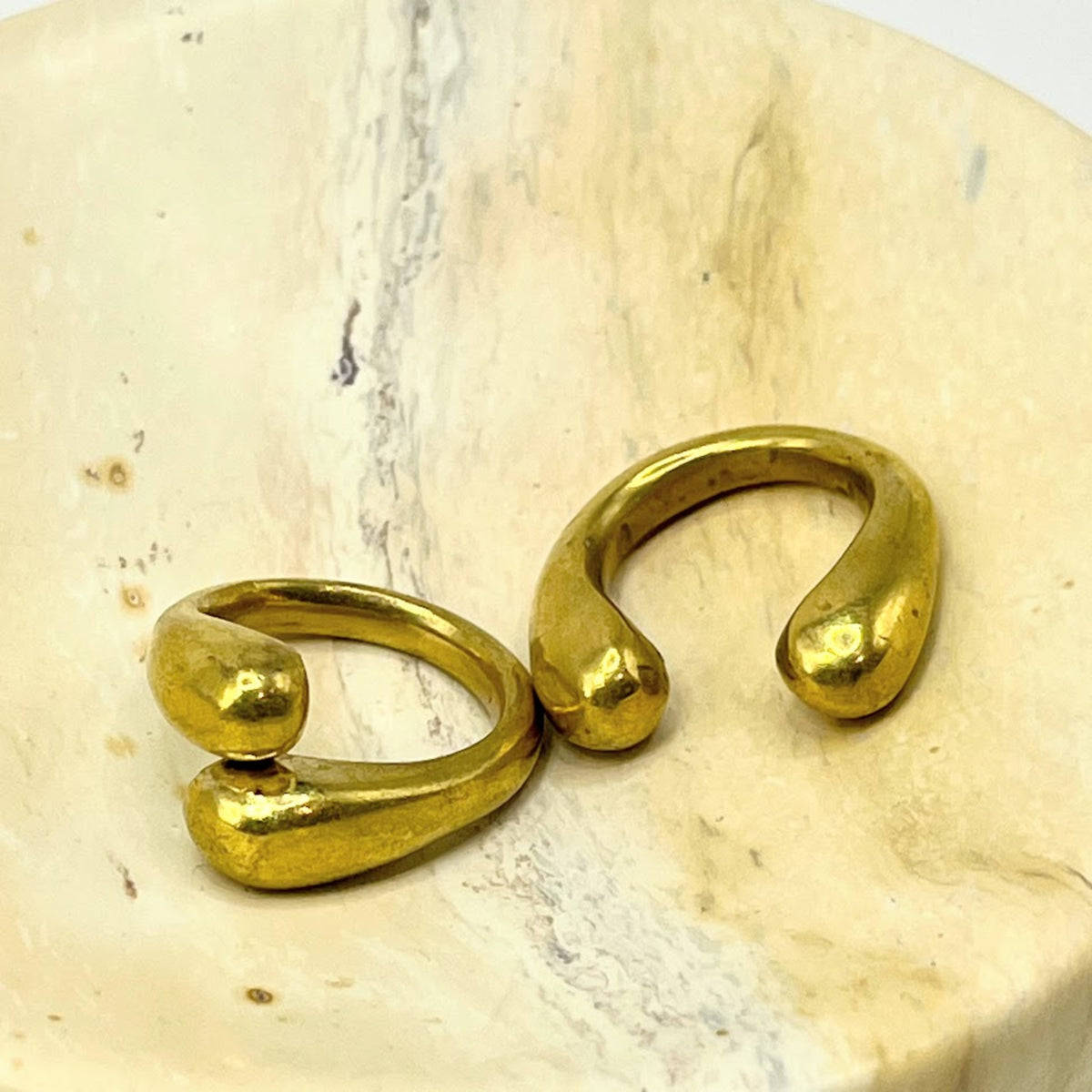 A pair of organic-shaped gold open cuff rings resting on a light beige stone surface.