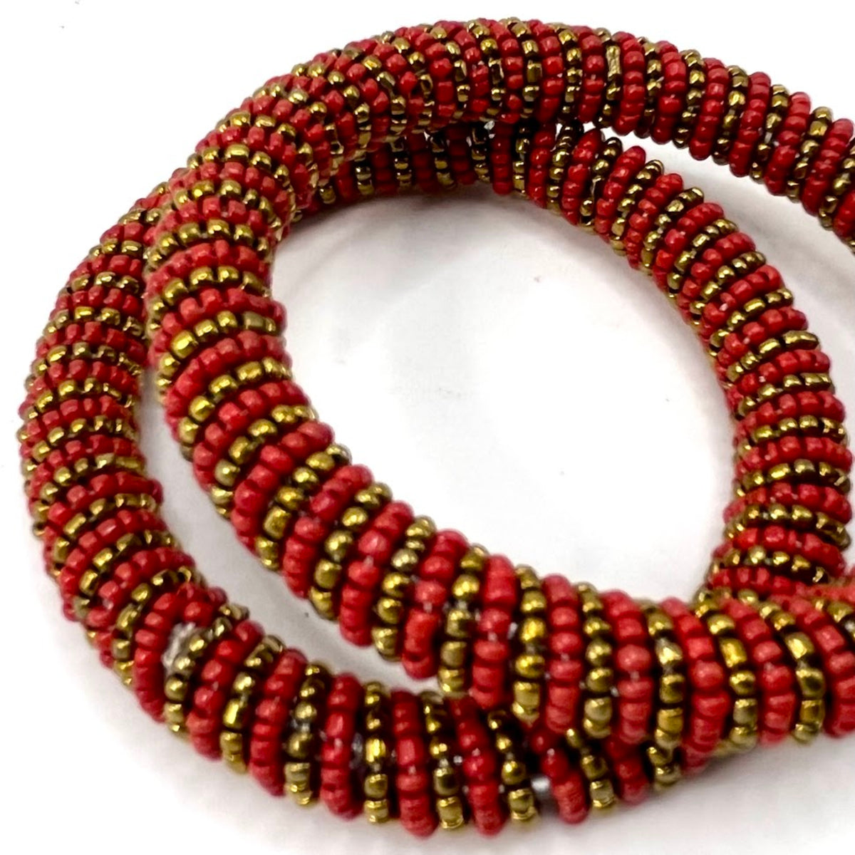 A coiled multi-strand beaded bracelet featuring alternating rows of textured red beads and metallic gold-finished seed beads, set against a plain white background.
