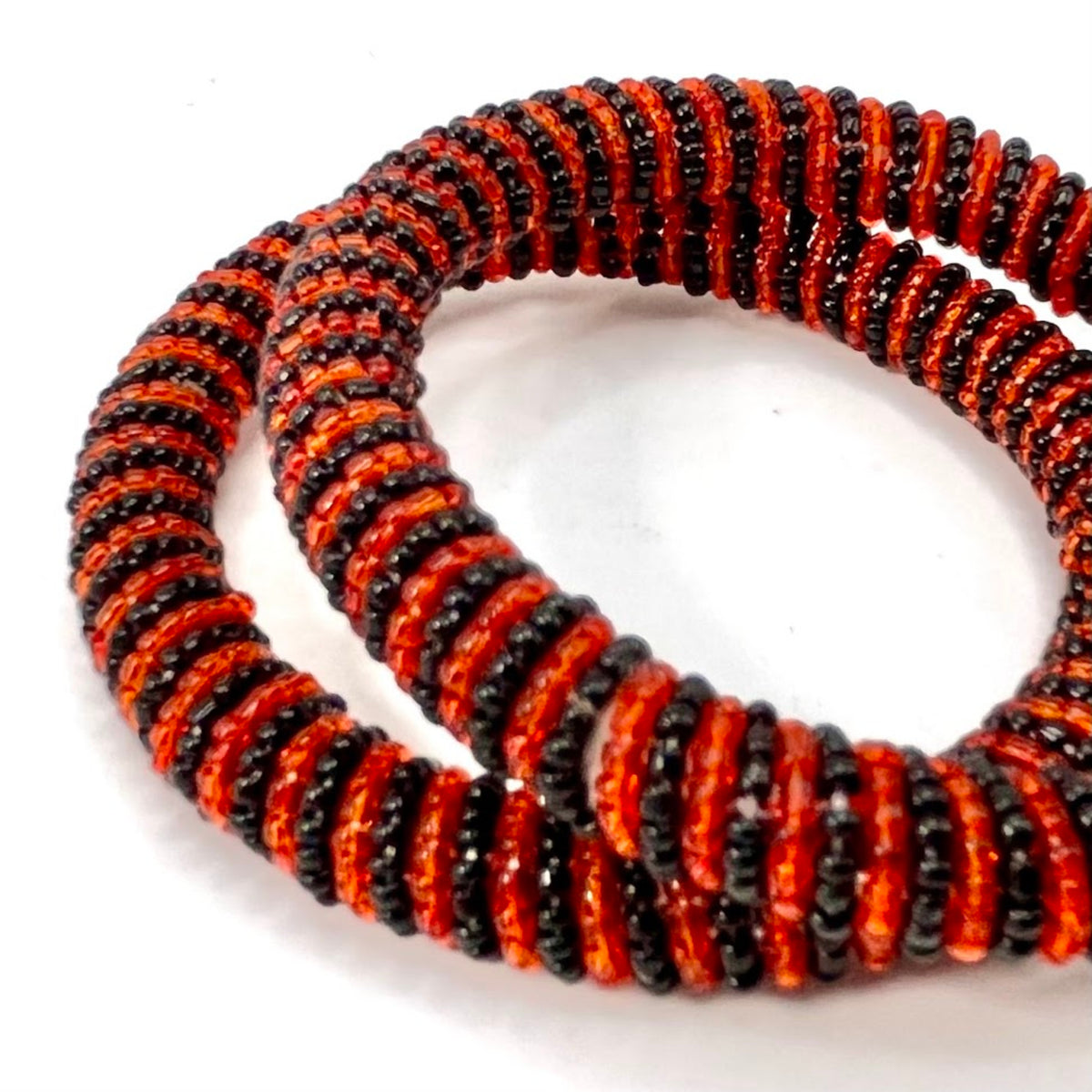A beaded stretch bracelet made of alternating red and black seed beads, coiled on a plain white background.